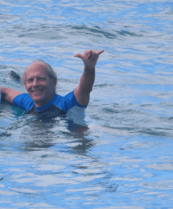 This was actually taken in the summer of 2019, but I'm going to do a lot of this in April 2020 too. Image of Doug Nordman surfing at White Plains Beach Oahu, giving a shaka sign from the water. | The-Military-Guide.com