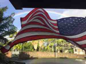 Image of American flag flying in the breeze beneath a rainbow in a Hawaii neighborhood as a metaphor for turbulence about the Financial Independence movement | The-Military-Guide.com