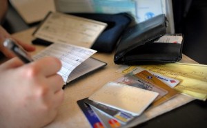Image of person paying the bills the old-fashioned way with a checkbook, wallet, and credit cards. Instead, put everything in autopilot. | The-Military-Guide.com