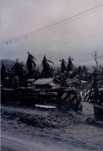Image of the Philippine town of Olongapo after the eruption of Mount Pinatubo, with the streets covered in ash and people walking alongside to check for survivors and damage. Palm trees were stripped by the wind. | MilitaryFinancialIndependence.com
