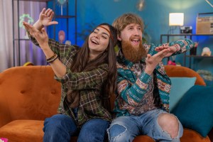 Image of a young hippie couple sitting on their livingroom couch pretending to waste their money by making it rain at the nightclub. | MilitaryFinancialIndependence.com