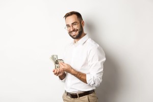 Image of smiling man holding a stack of cash, contemplating his future freedom during his new life of financial independence. | MilitaryFinancialIndependence.com